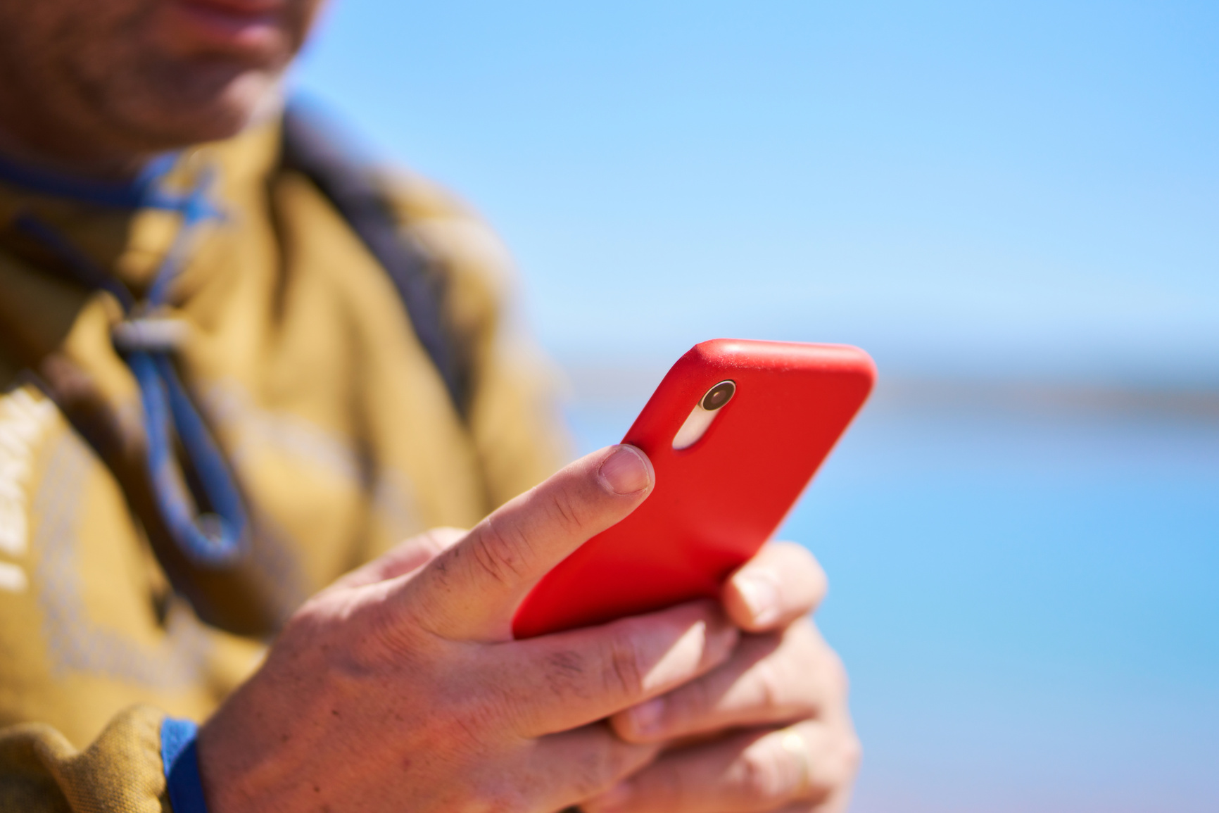 an unrecognizable man looking at his cell phone on a lake shore